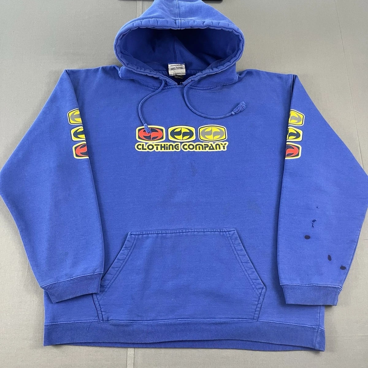 A blue hoodie with yellow and red graphics is laid flat on a gray surface.