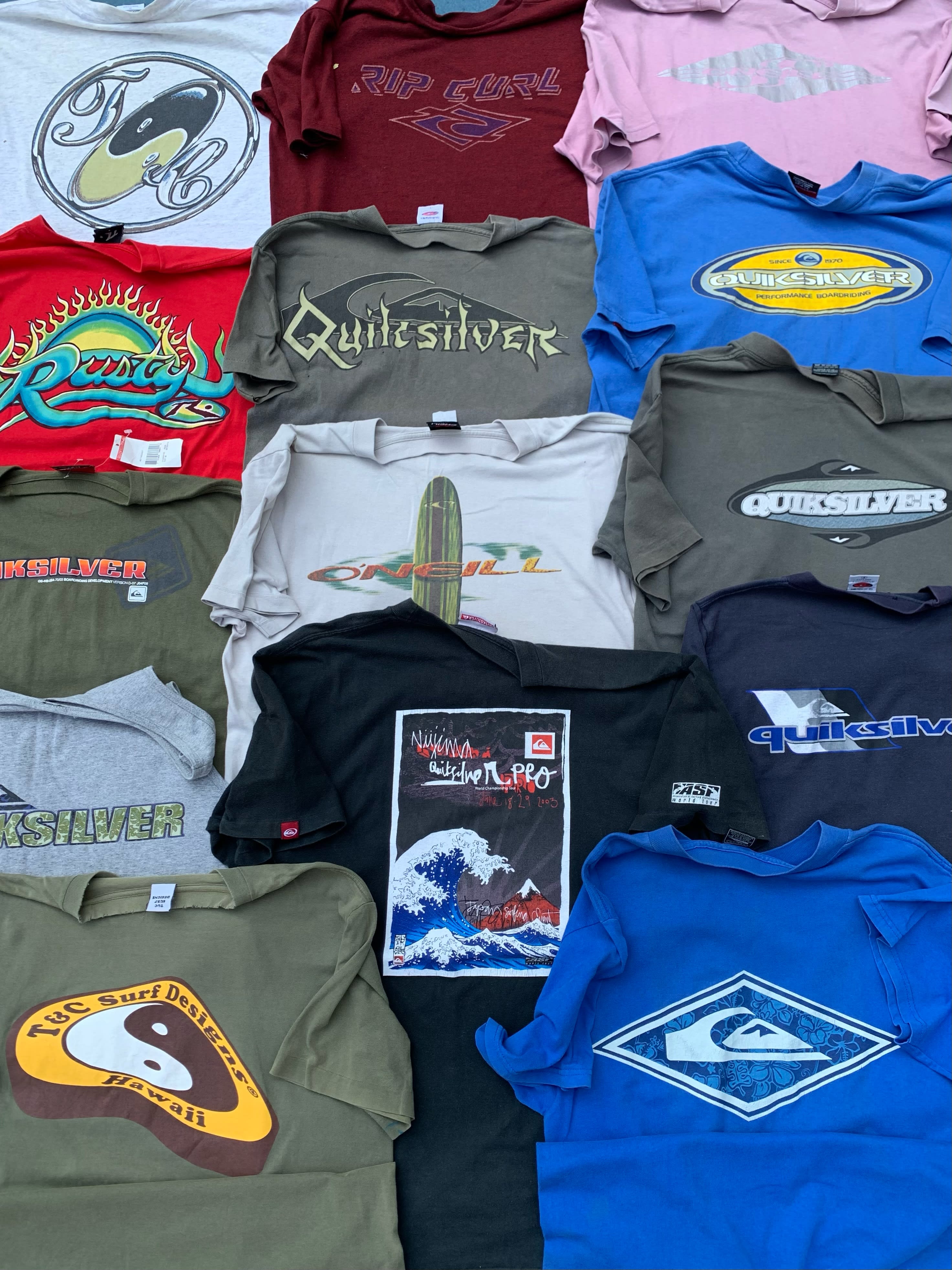 A collection of colorful surf-brand t-shirts is spread across a neutral-toned background.