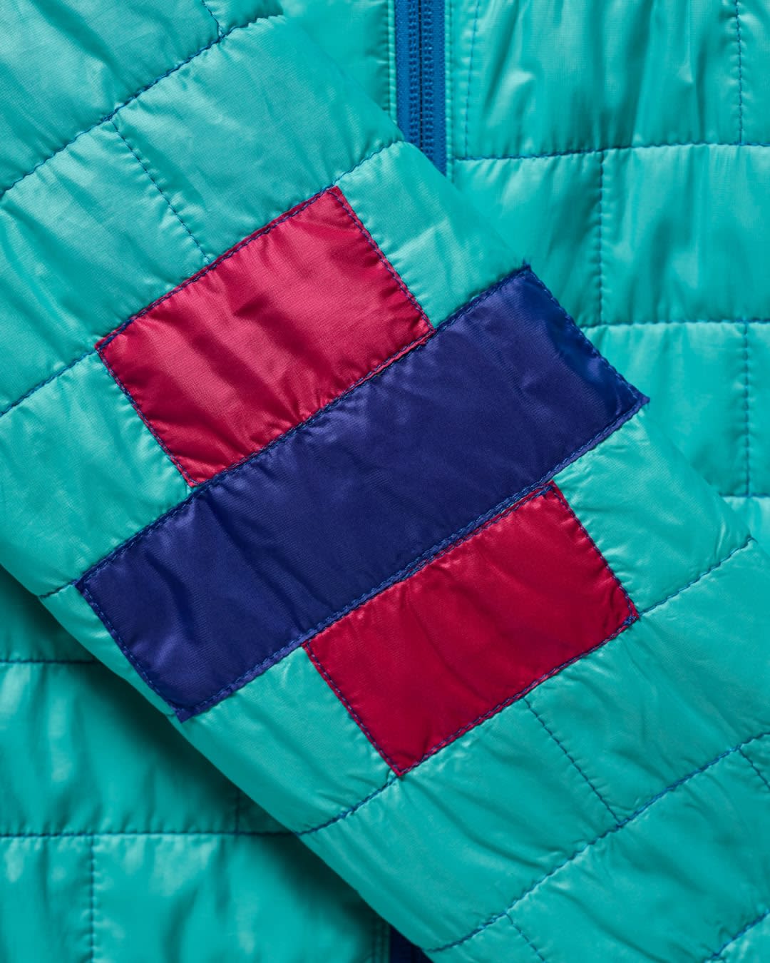A close-up of a quilted turquoise jacket sleeve features a patch of red and blue squares and rectangles.