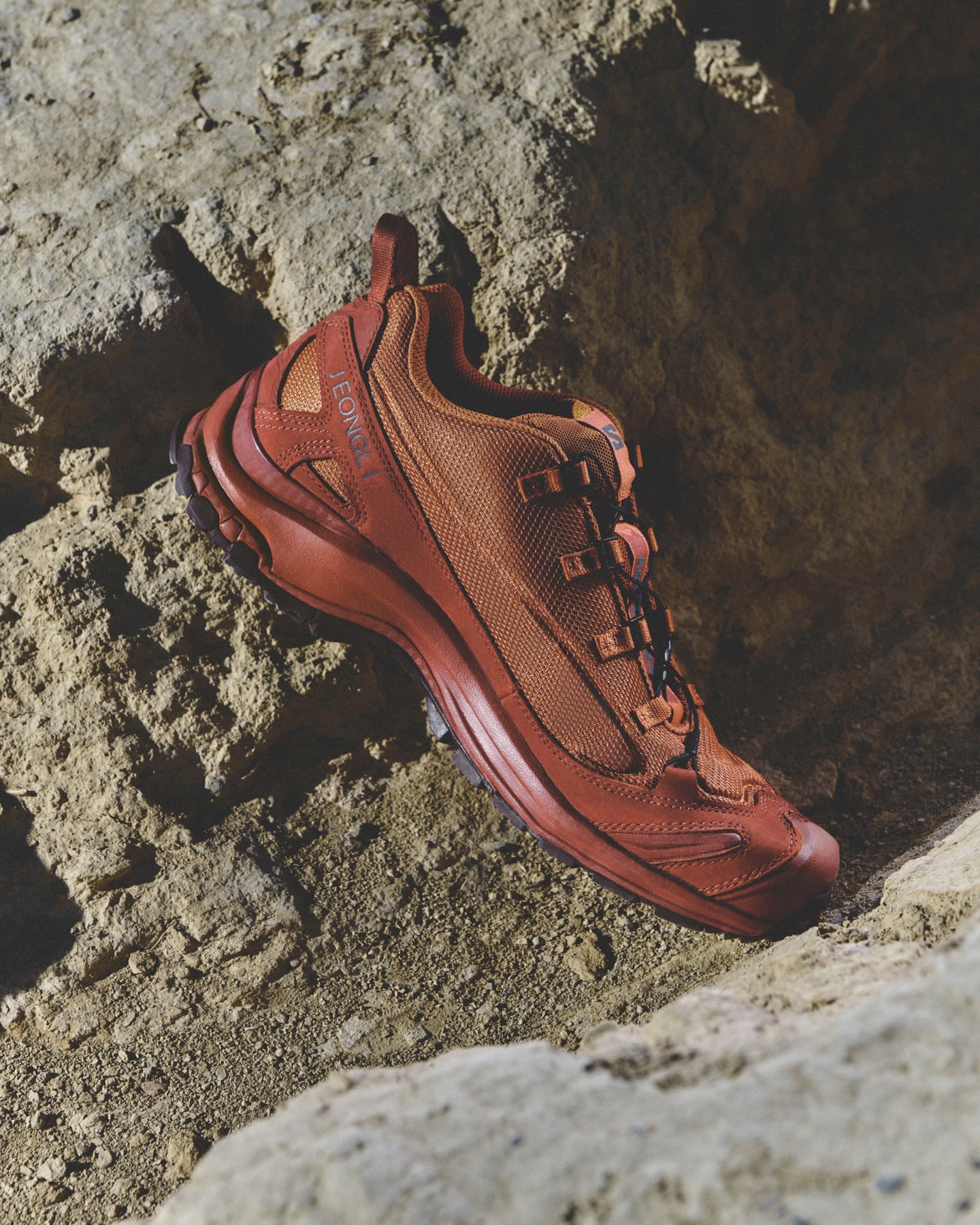 A single orange hiking boot rests on a rugged, rocky terrain.