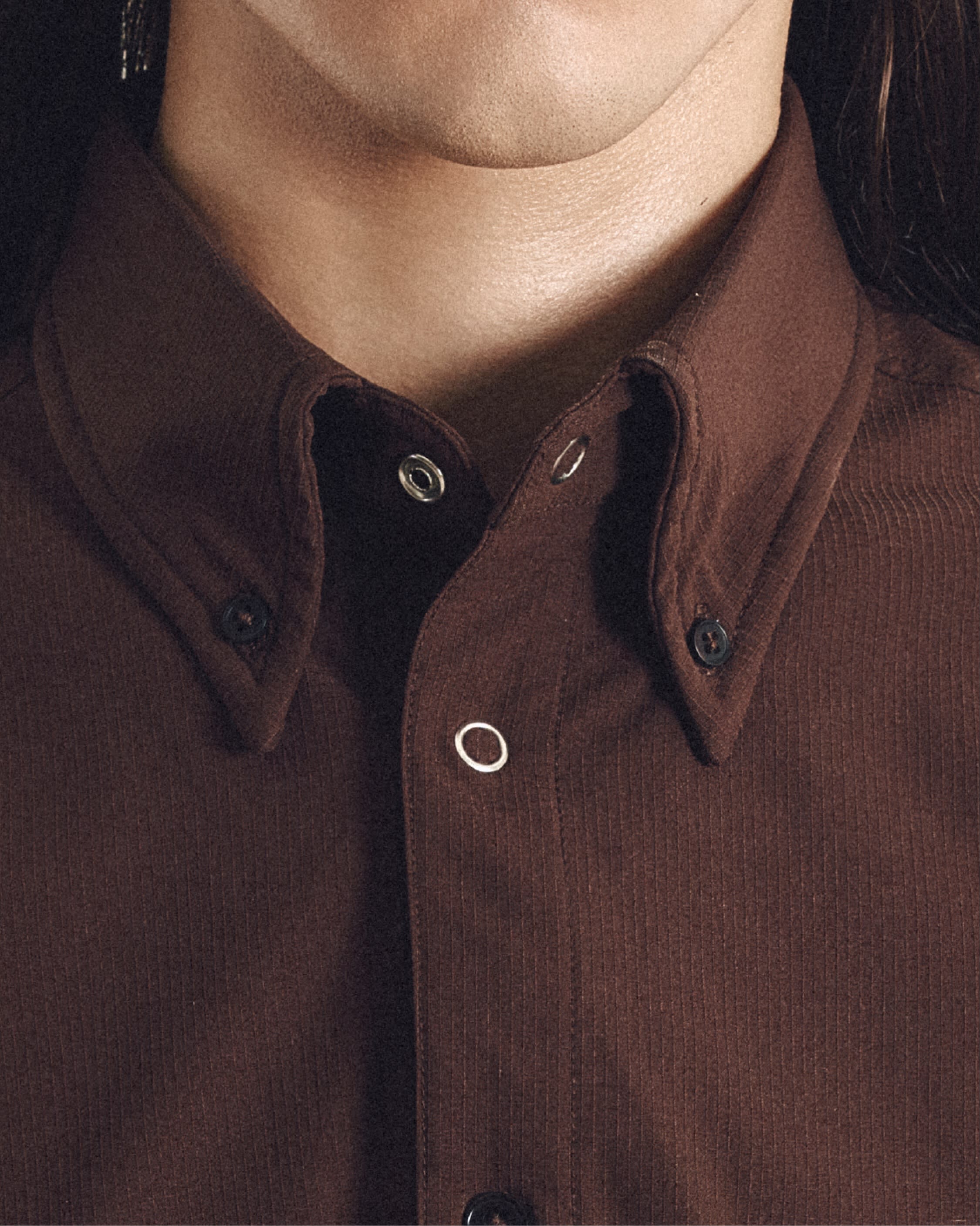 A close-up of a person's neck and chin in the background, wearing a brown corduroy button-down shirt in the foreground.