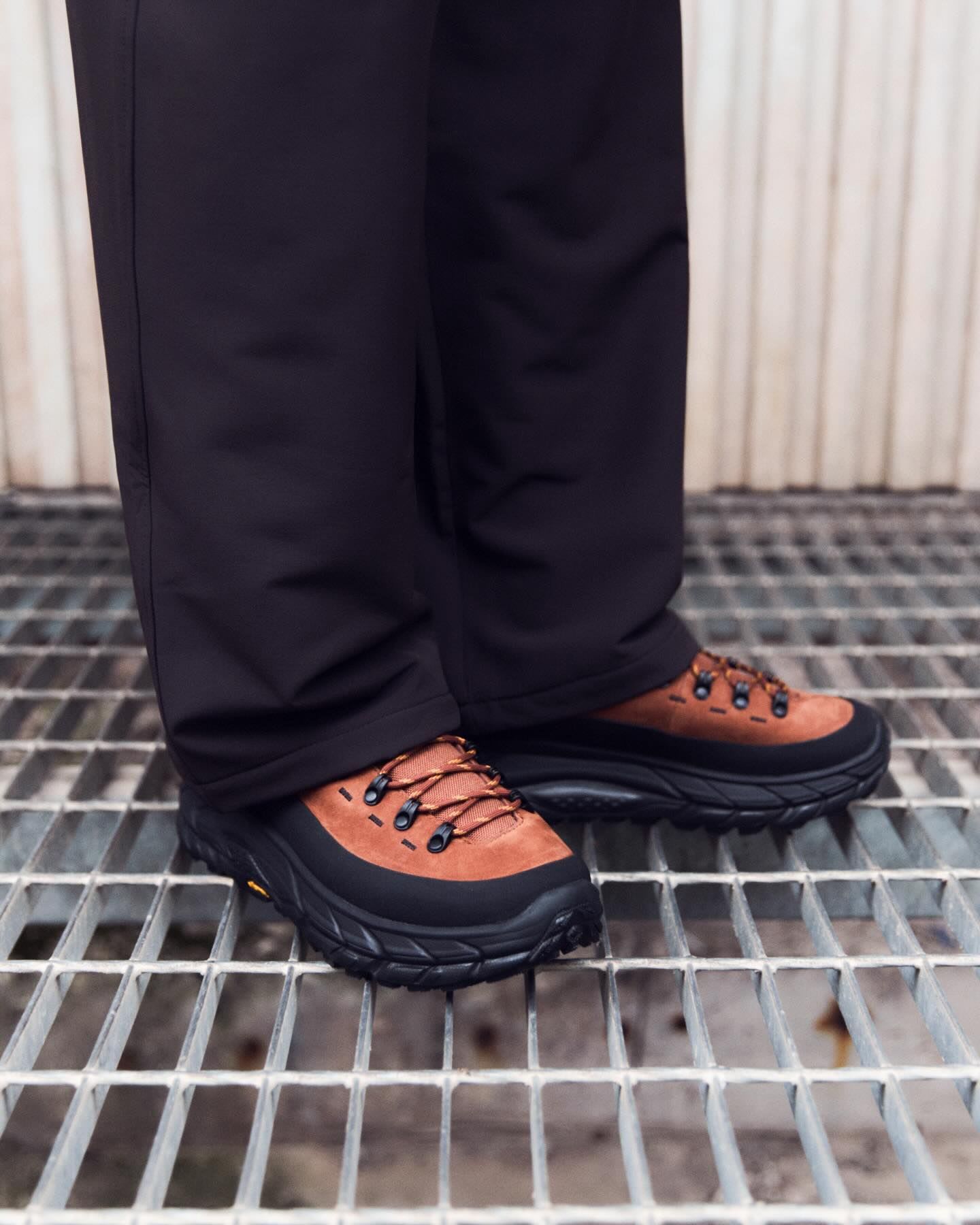 Legs in black pants and brown and black hiking shoes standing on a metal grate.