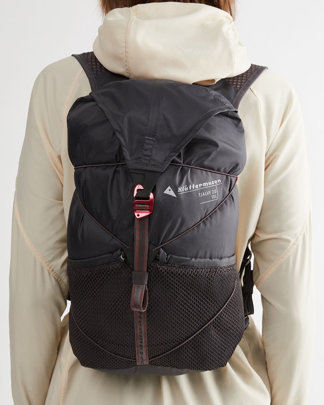 Rear view of a person wearing a black Klättermusen TJALVE 2.0 10L backpack with red details and mesh pockets.