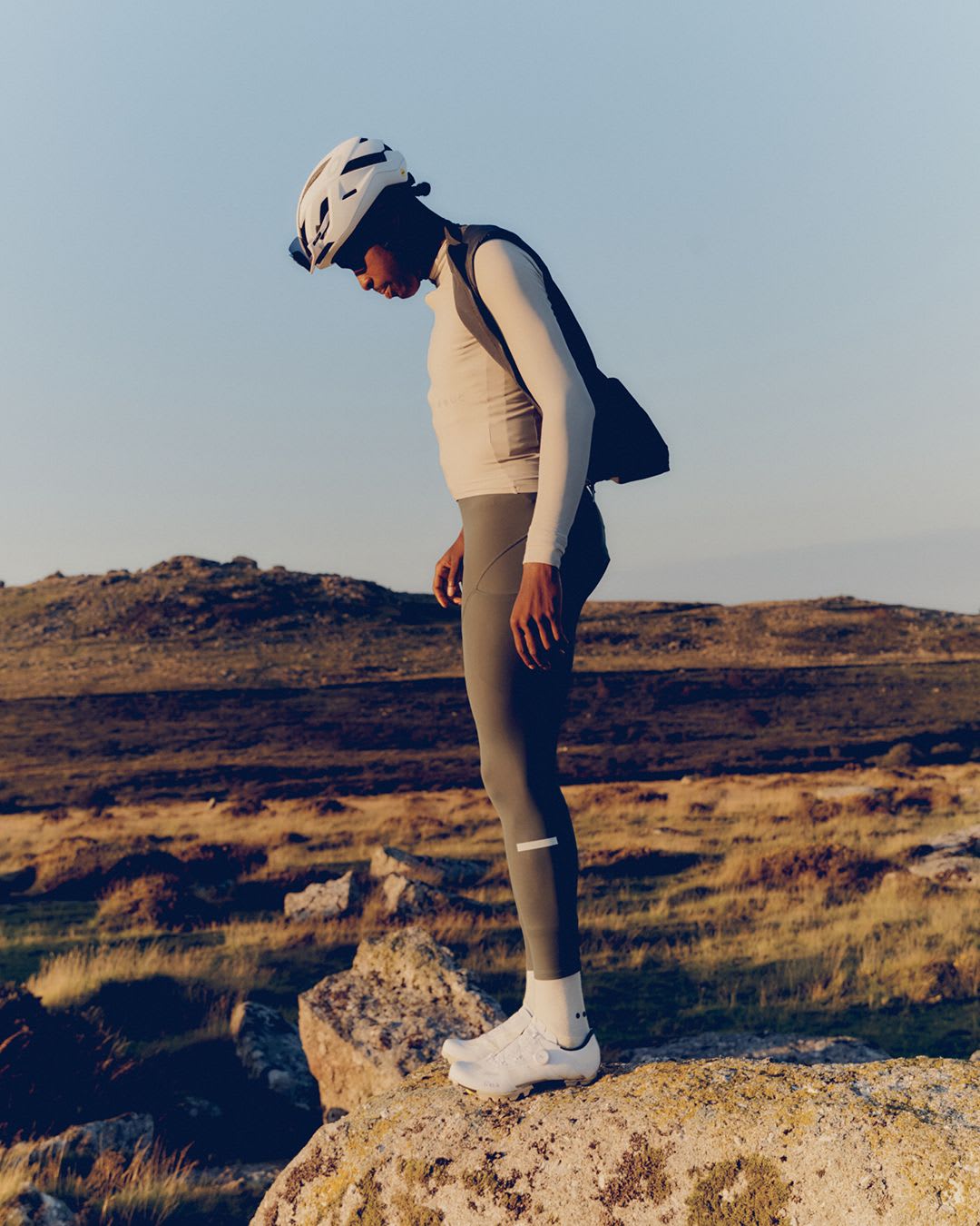 A person in cycling gear and helmet stands on a rock, looking down, in a rocky outdoor landscape.