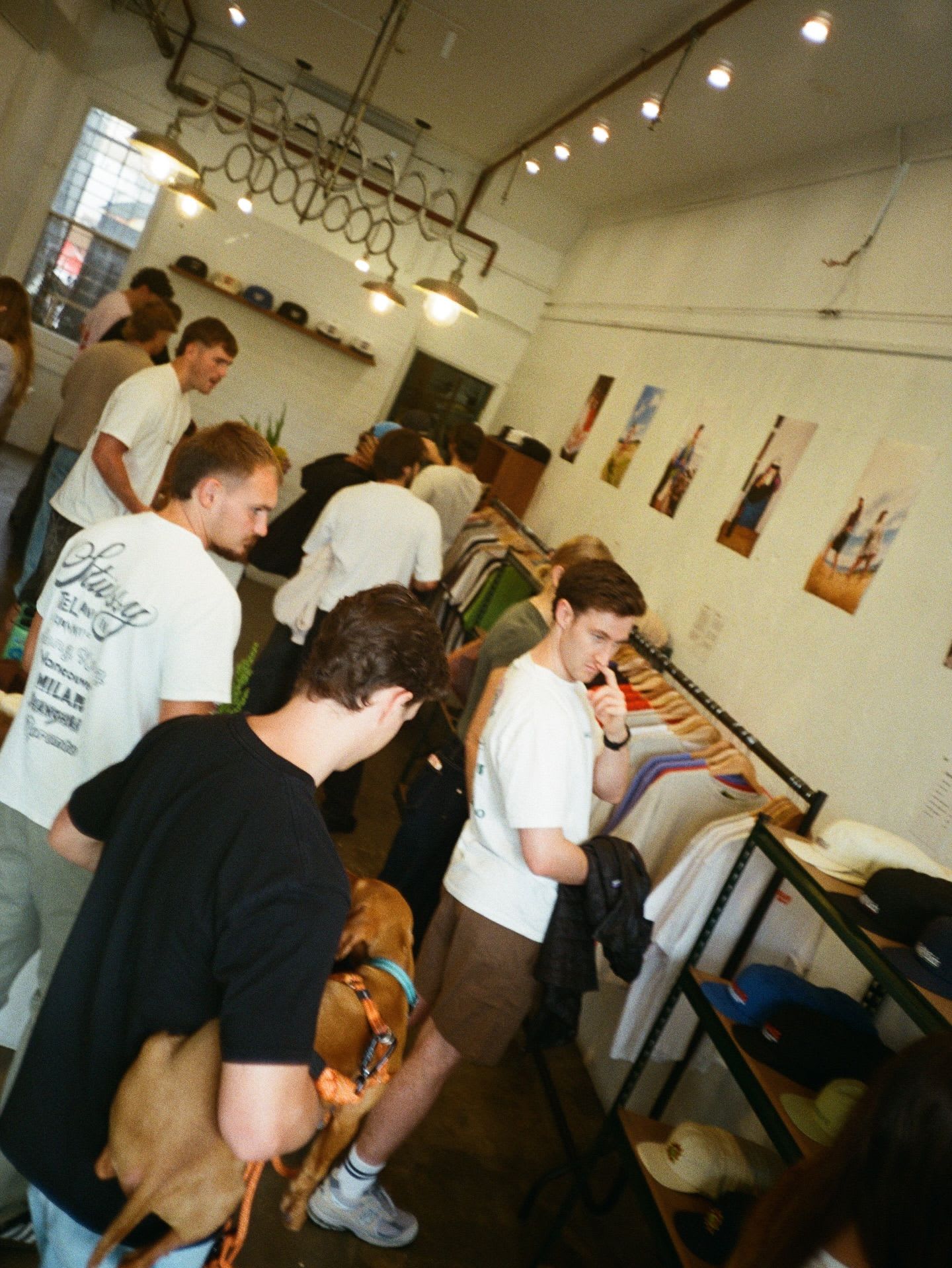 A group of people browsing clothing in a store, with one person holding a brown dog.
