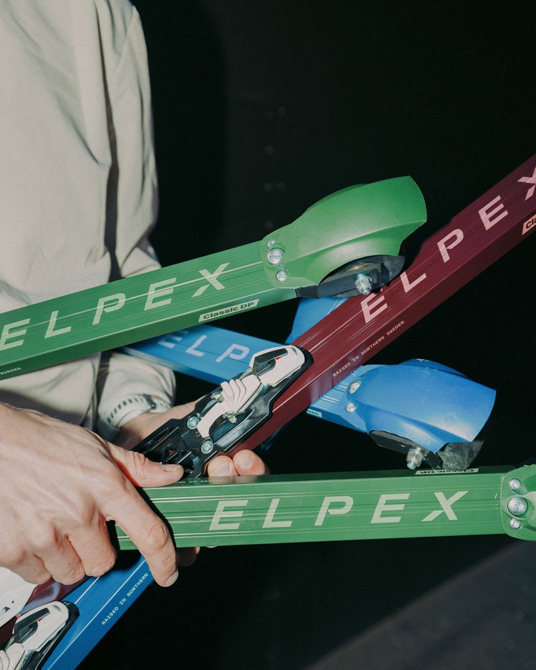 A person's hands hold multiple green, red, and blue ELPEX roller skis.