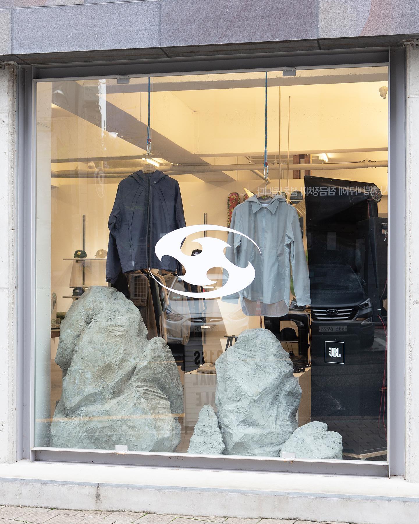 Large grey rocks sit in the foreground of a store window, with clothing displayed on hangers in the background.