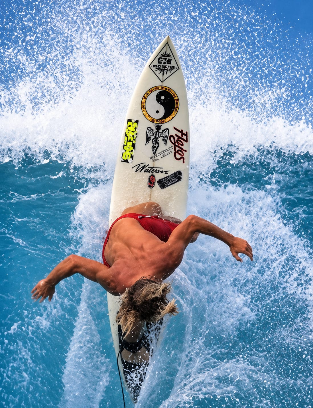 A shirtless man in red swim trunks falls backward off a white surfboard into crashing blue ocean waves.