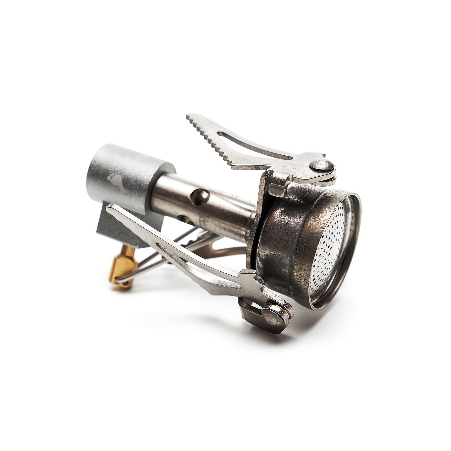 A small, metallic portable camping stove sits centered against a plain white background.