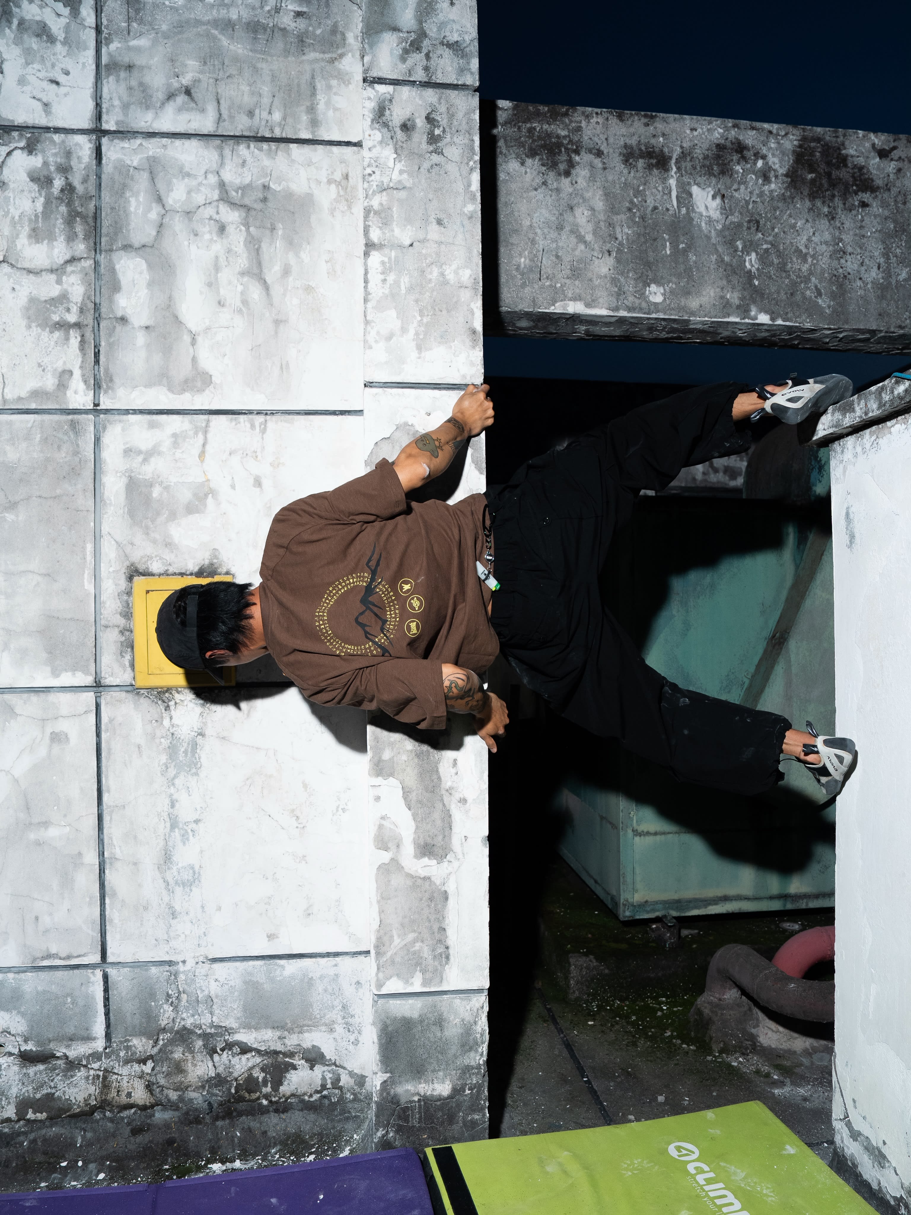 A man in a brown shirt and black pants climbs a concrete wall against a dark night background.