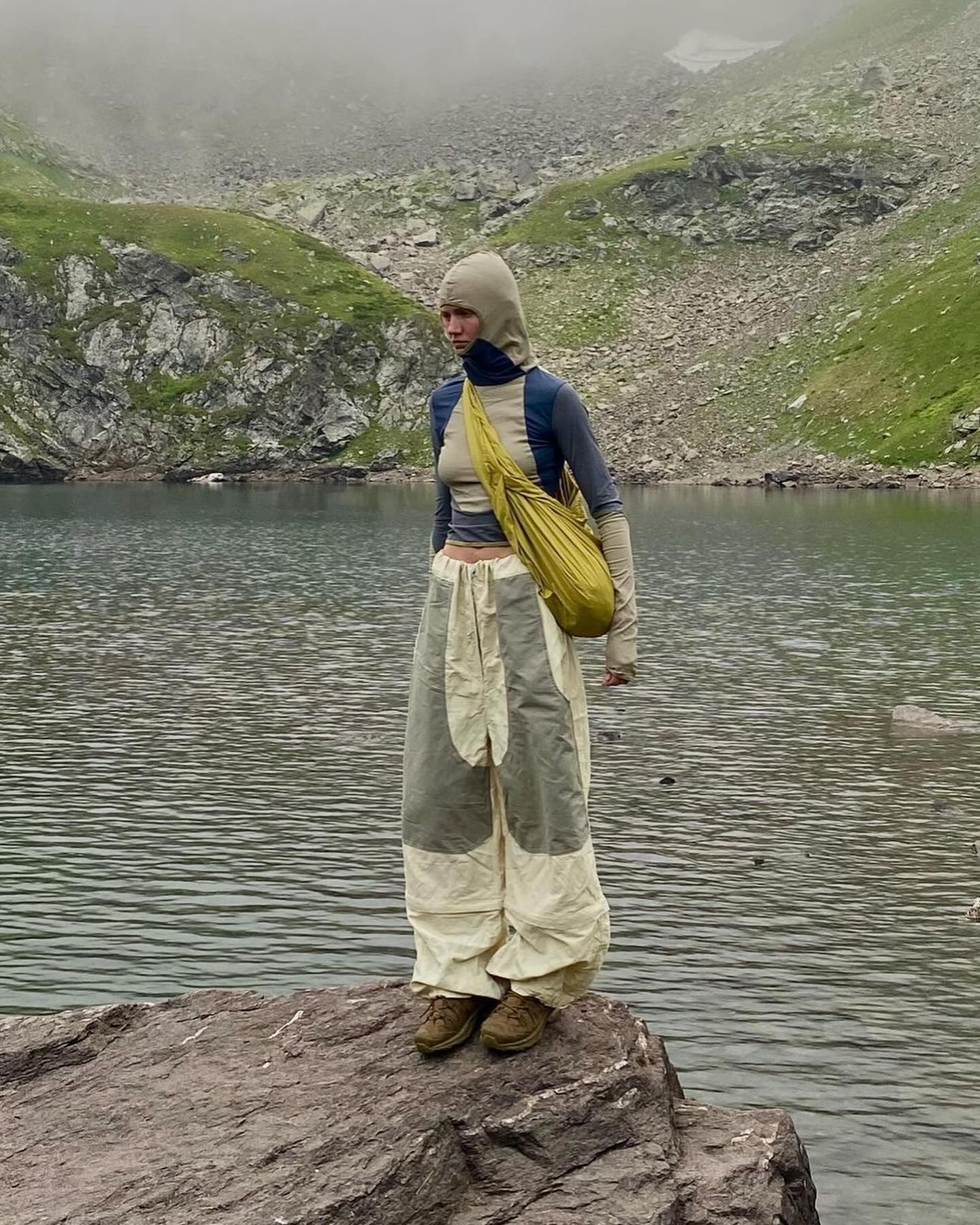 A person stands on a rock in the foreground, with a calm lake and misty mountains in the background.