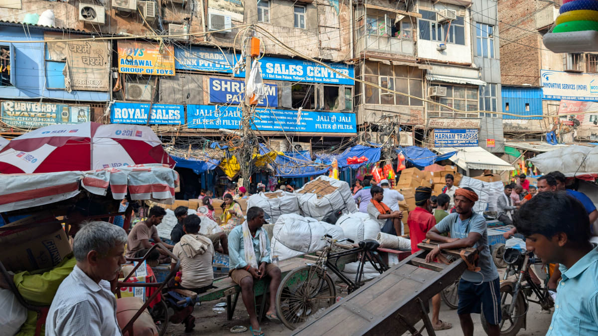 A crowded market street in Old Delhi with rows of shop signboards, handcarts and shoppers.