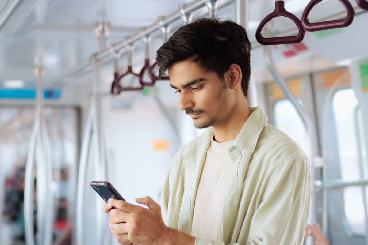A young man standing on a metro train, scrolling on his smartphone.