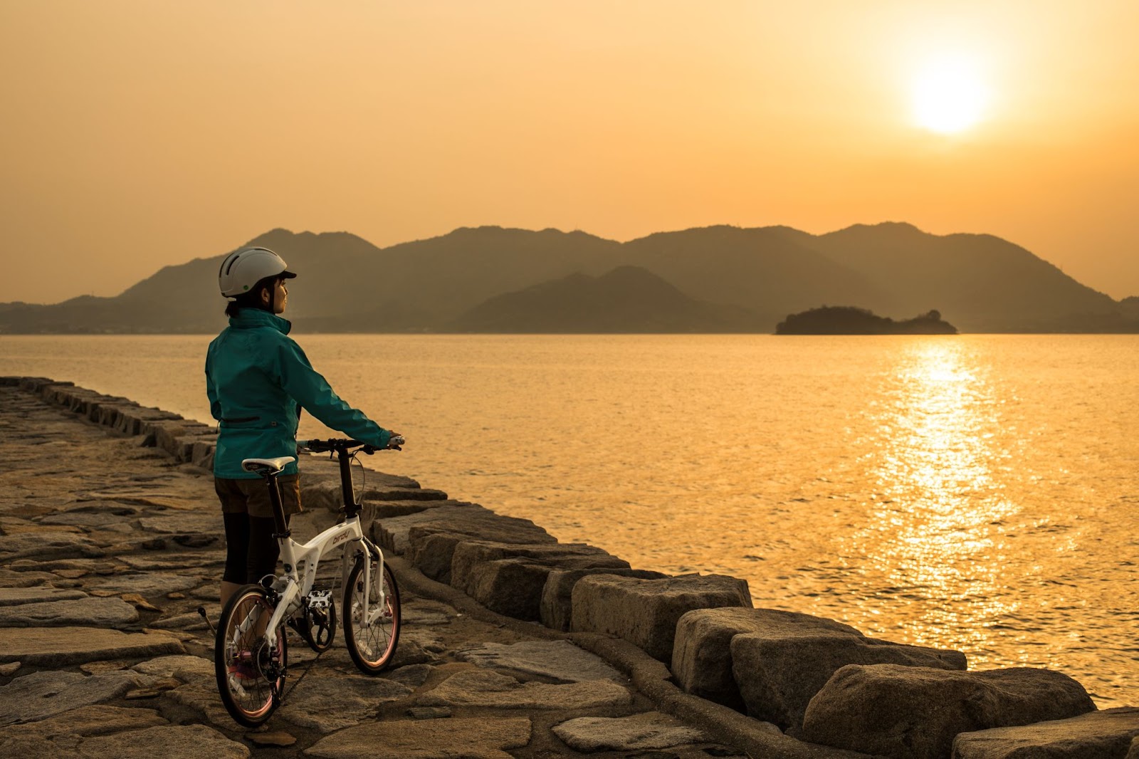 A person standing on a rock with a bicycle by the waterDescription automatically generated