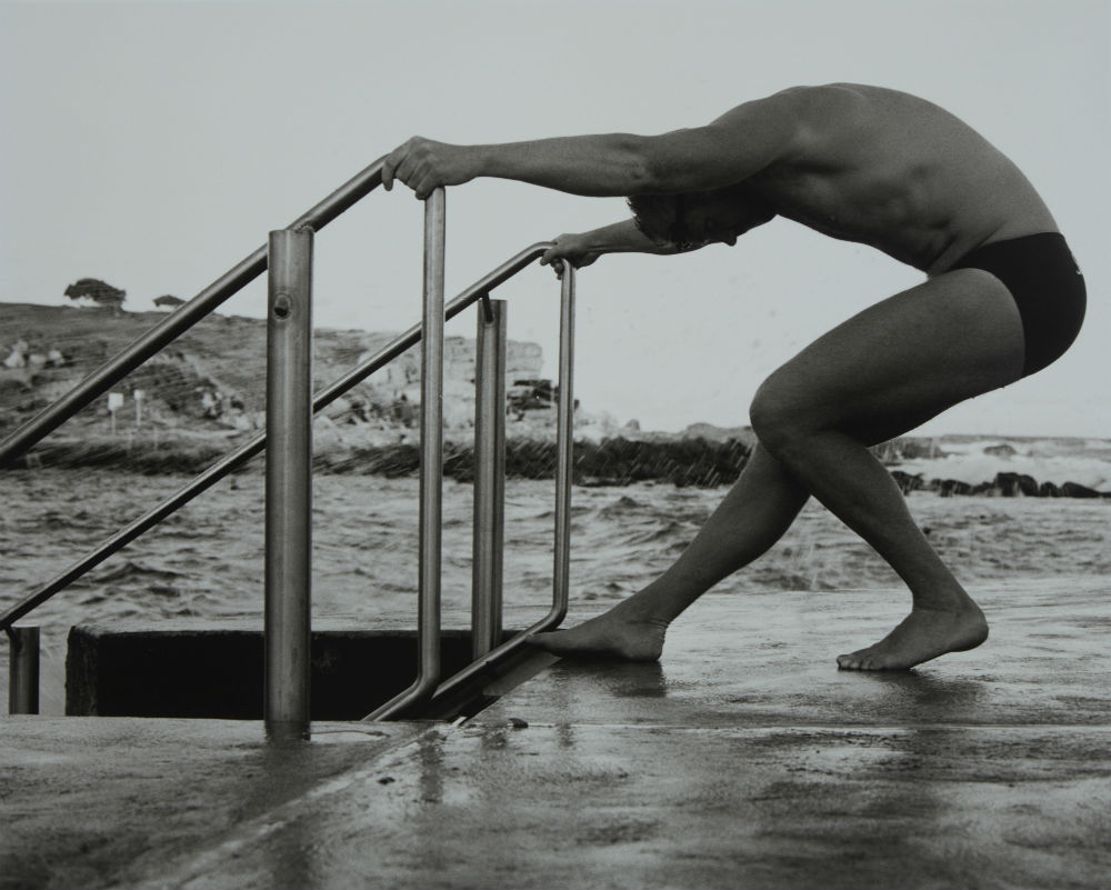 A person in a swimsuit leaning on a metal railingDescription automatically generated