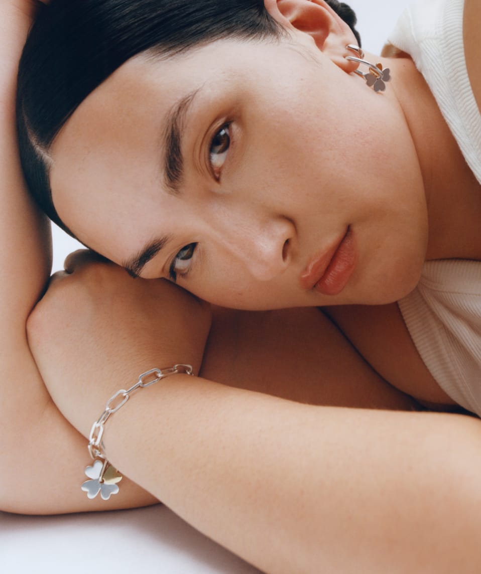 Model is resting her head on her arm and looking into the camera. She is wearing the Mejuri X Ganni bracelet. 