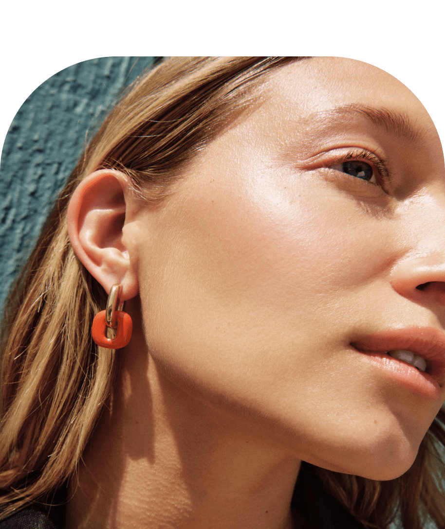 The model is wearing the Stevie Hoops in Red Enamel. Her face is turned to the side and she is standing against a teal wall. The image is zoomed in and you can see her jawline.