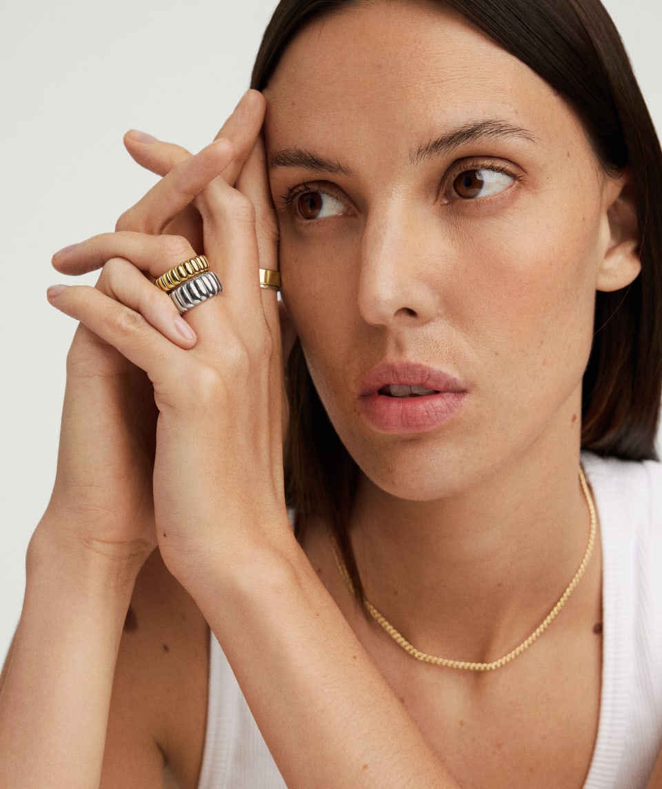Model has her hands lightly clasped resting against her face. She is looking to the side. She is wearing the Charlotte Bold and Slim rings stacked together. Creating a mixed metal look. 