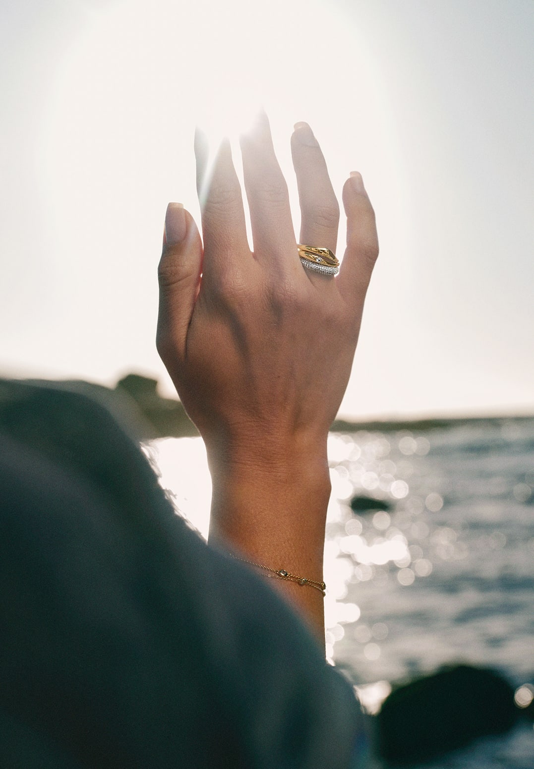 Hand wearing a stack of rings against the backdrop of a beach at sunset
