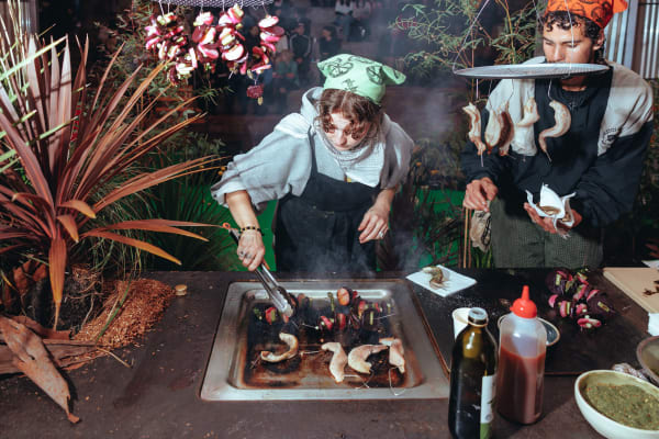Two people cooking prawns on an outdoor grill.