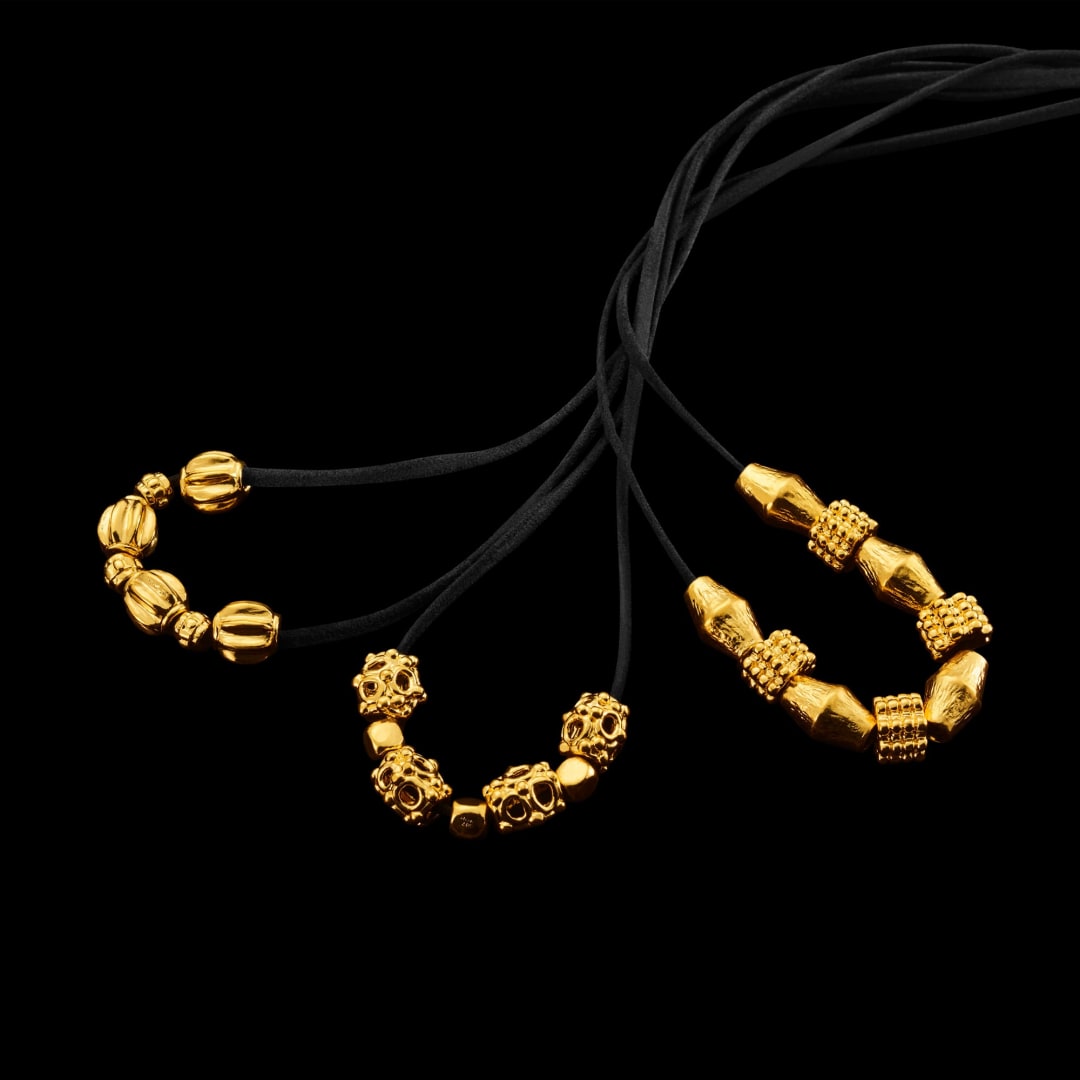 The Menē Ancient Beads Collection in pure 24k gold and pure platinum, including the Wavy Bead, Ancient Bead, Wheel Bead, and Textured Long Bead.