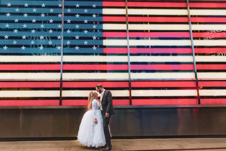 bride wearing big white dress by the American flag in Times Square 