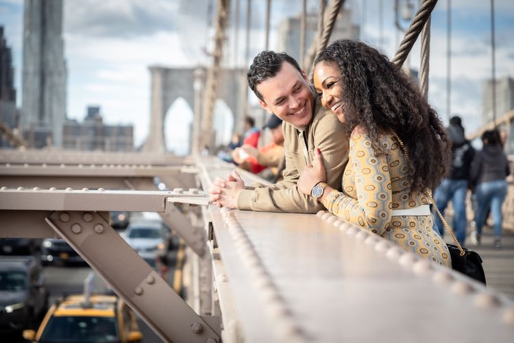 interracial couple smiling and holding hands on the Brooklyn Bridge in New York City on a cloudy day 