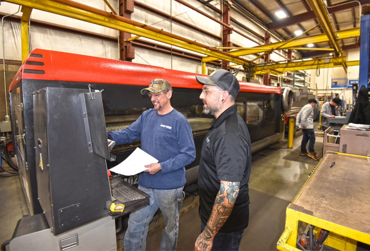 Two metal fabricators working on laser cutting machine