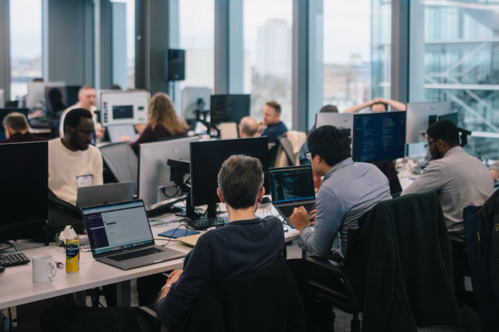 An engineering team working at desks with laptops and monitors in a bright London office with floor-to-ceiling windows