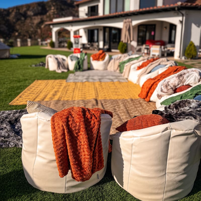 Backyard lounge with white bean bags, orange and green throws, and layered rugs