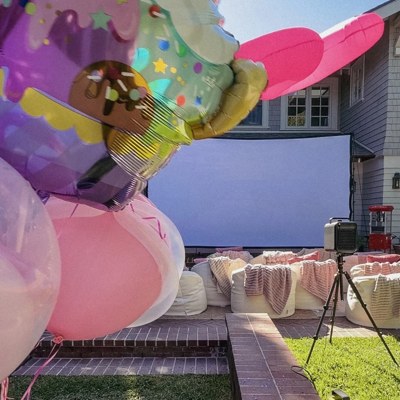 Birthday balloons beside a backyard cinema with pink throws and white bean bags