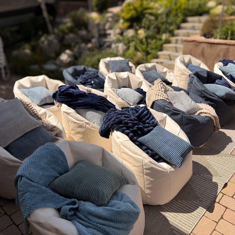 Rows of white and blue bean bags with cushions and textured throws on a patio