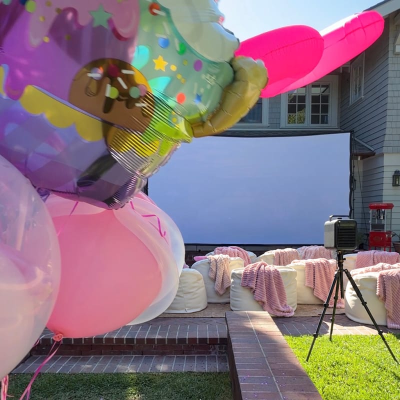 Birthday balloons beside a backyard cinema with pink throws and white bean bags