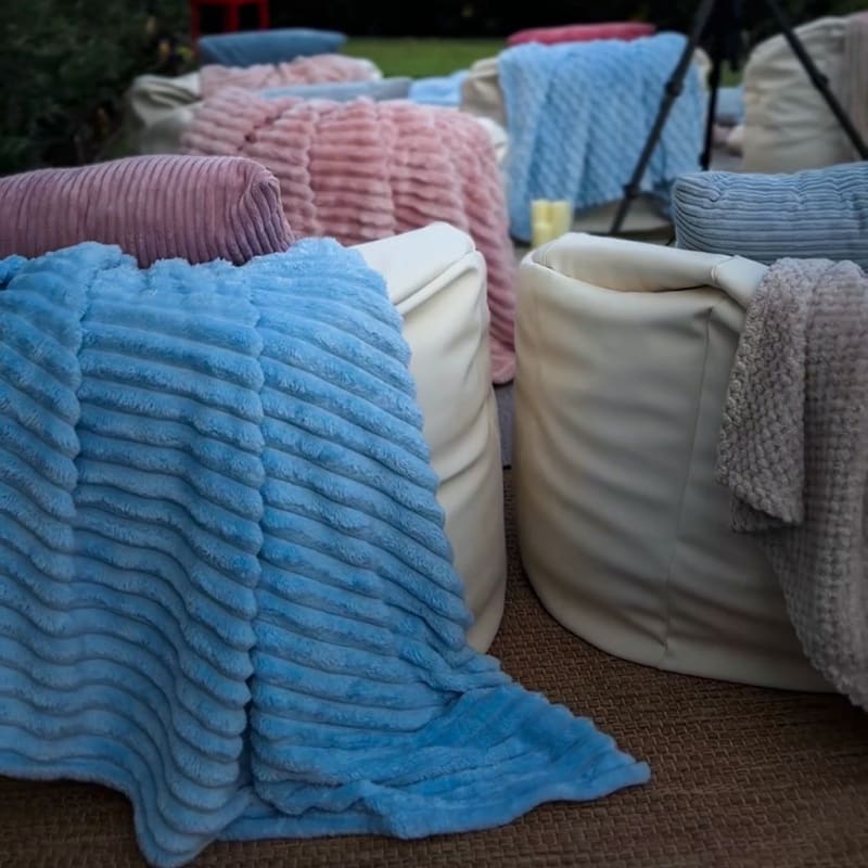 White bean bags layered with blue, pink, and gray textured throws for an outdoor movie night