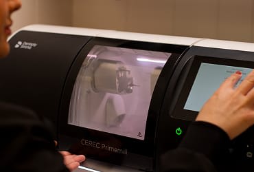 A dental technician interacting with the CEREC machine creating a same-day crown.