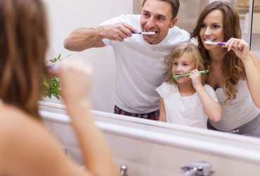 A family reflected in a mirror as they brush their teeth.