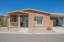 Salmon coloured manufactured home with a covered front porch, railing and attached carport