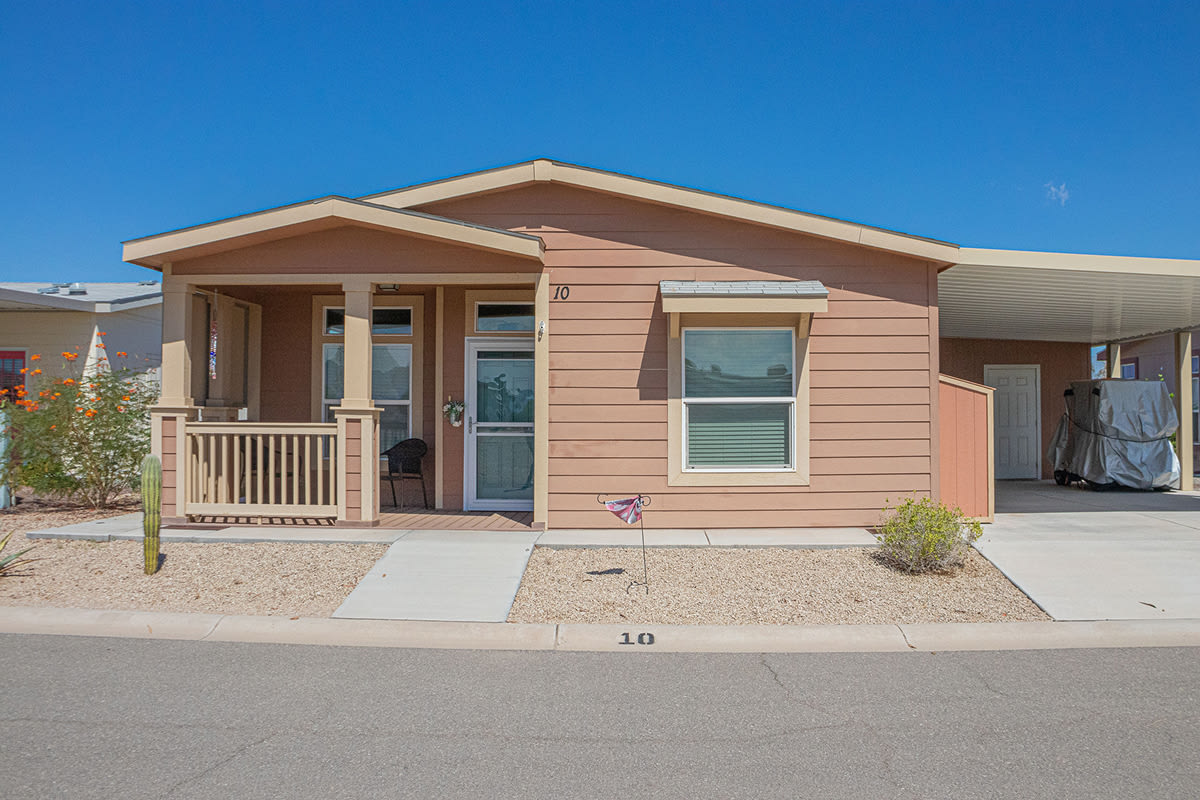 Salmon coloured manufactured home with a covered front porch, railing and attached carport