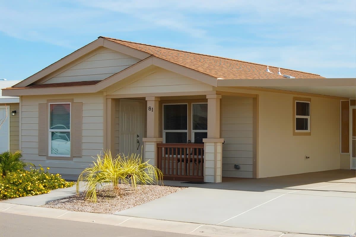 Cream and tan manufactured home with a columned porch and flowering shrubs beside the walkway
