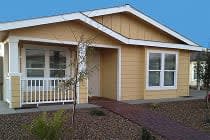 Golden yellow manufactured home with white porch railing and a brick paver walkway