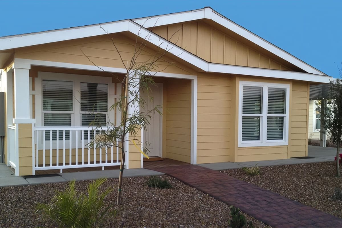 Golden yellow manufactured home with white porch railing and a brick paver walkway