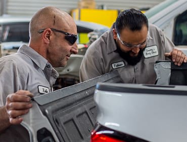 Two workers inspecting the tailgate of a pickup truck.
