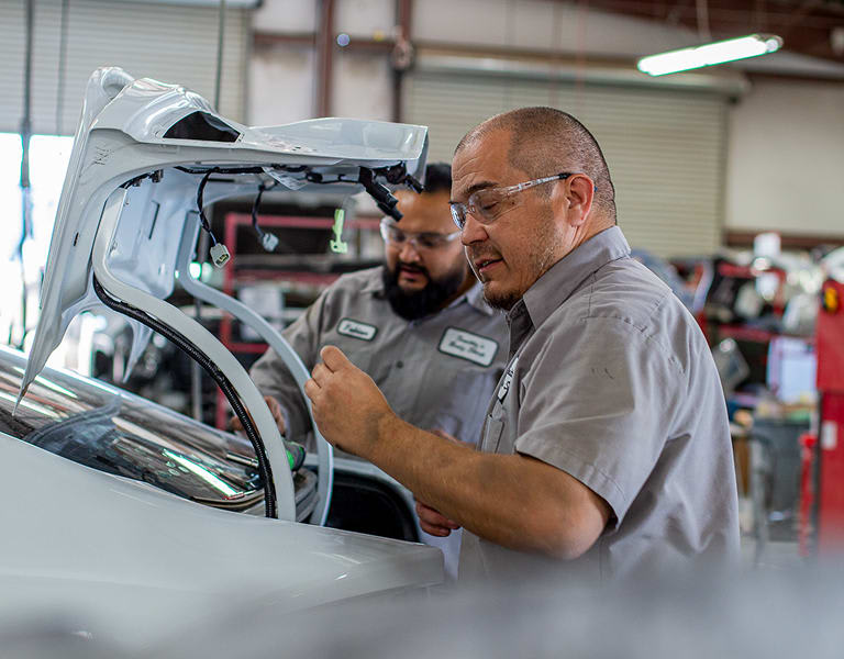 Two Smitty's employees working on the trunk of a car.