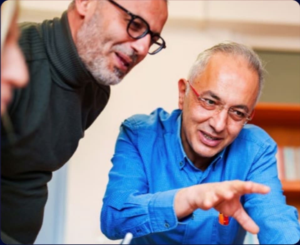 Two men in glasses looking at something together, one pointing as he explains it