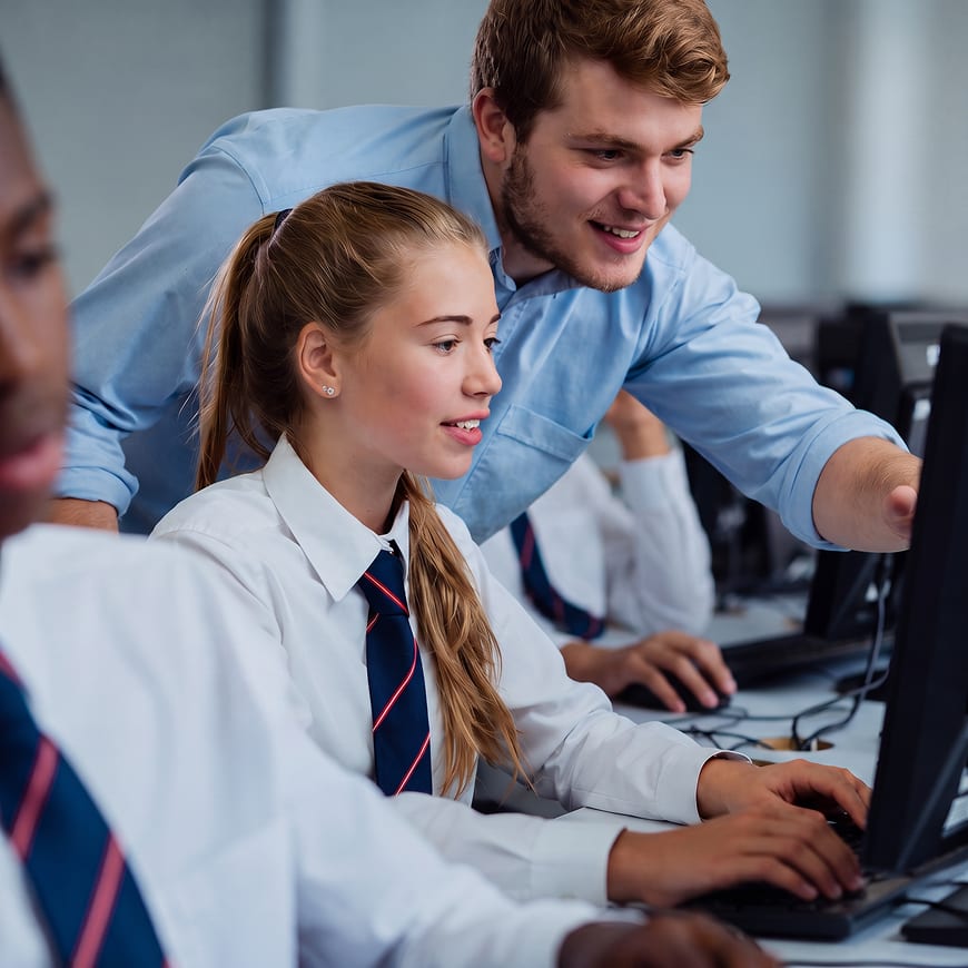 Male teacher assisting a secondary school student at a computer.