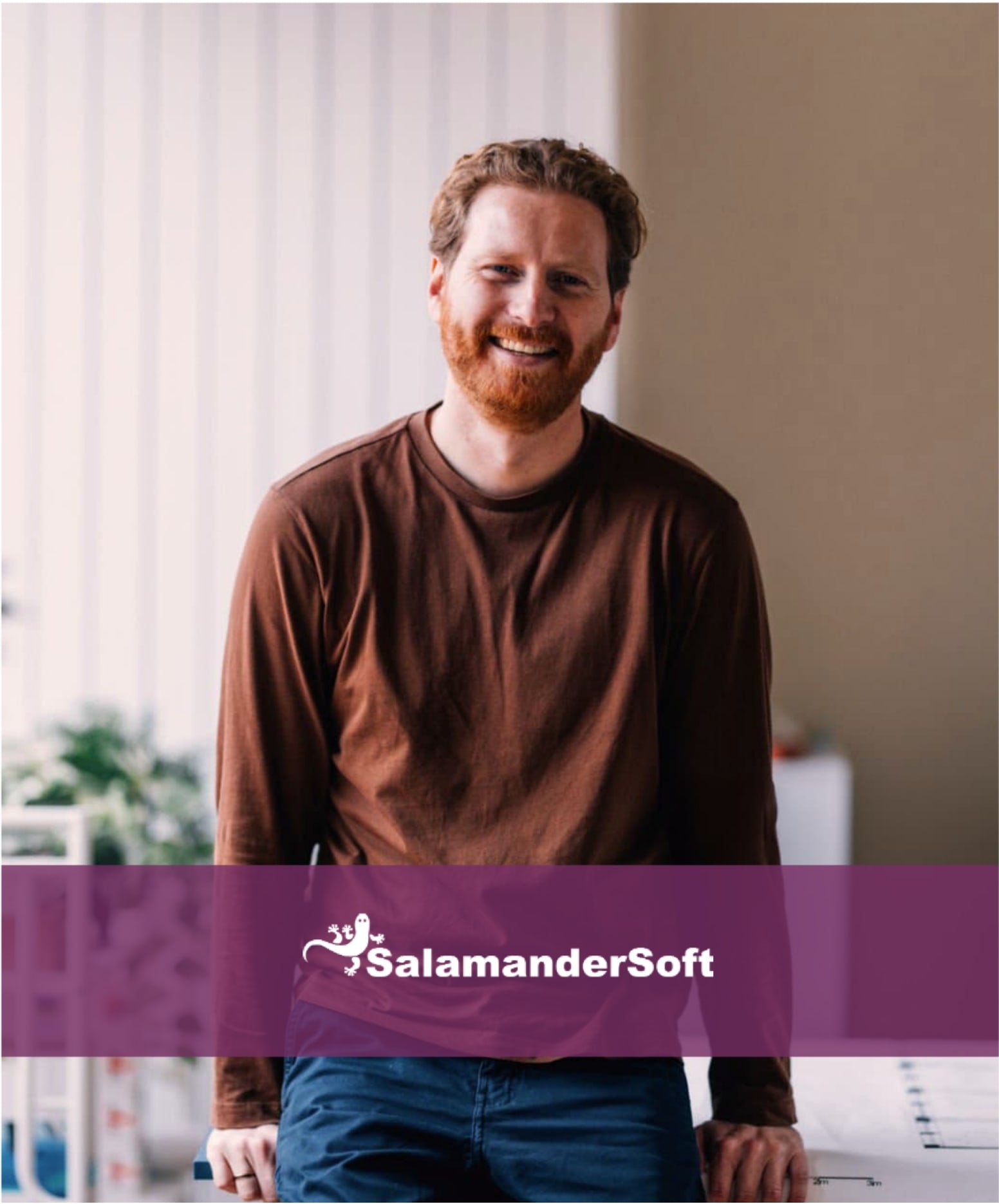 Smiling man with red hair and a beard standing in a bright office.