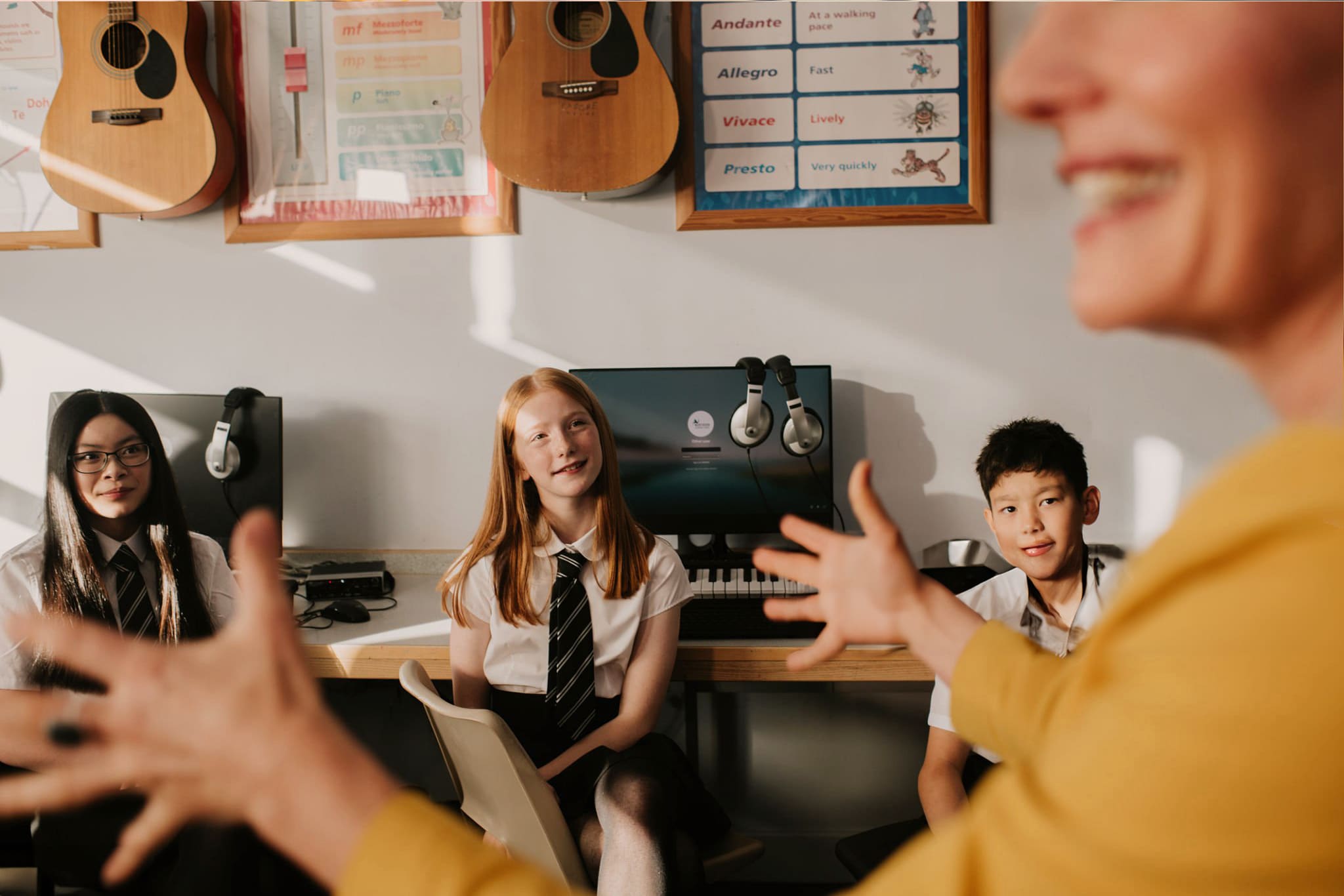 A female teacher gestures enthusiastically while teaching secondary school students in a music tech classroom.