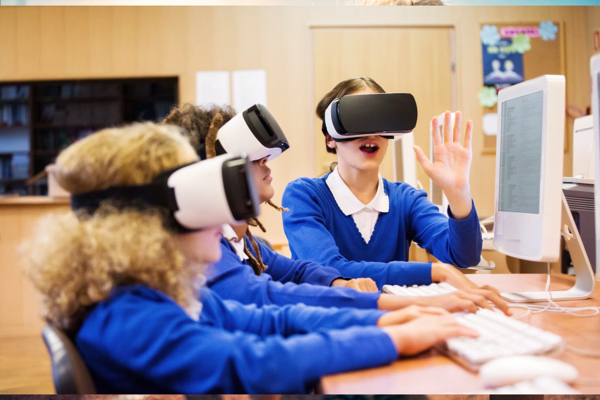 Schoolchildren wearing VR headsets while seated at desktop computers in a classroom.