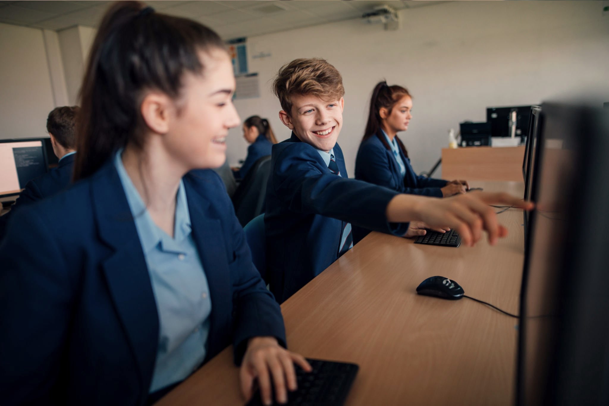 Smiling pupils in navy blazers working at computers in a school IT suite