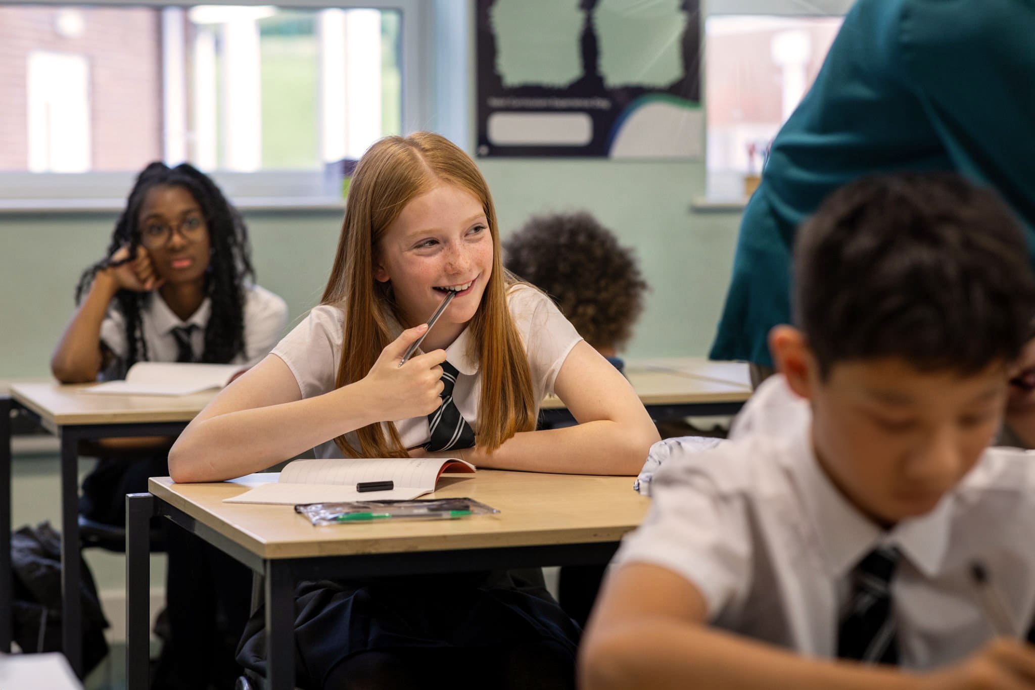 Secondary pupils in white shirts and striped ties work at desks in a bright classroom, one girl smiling